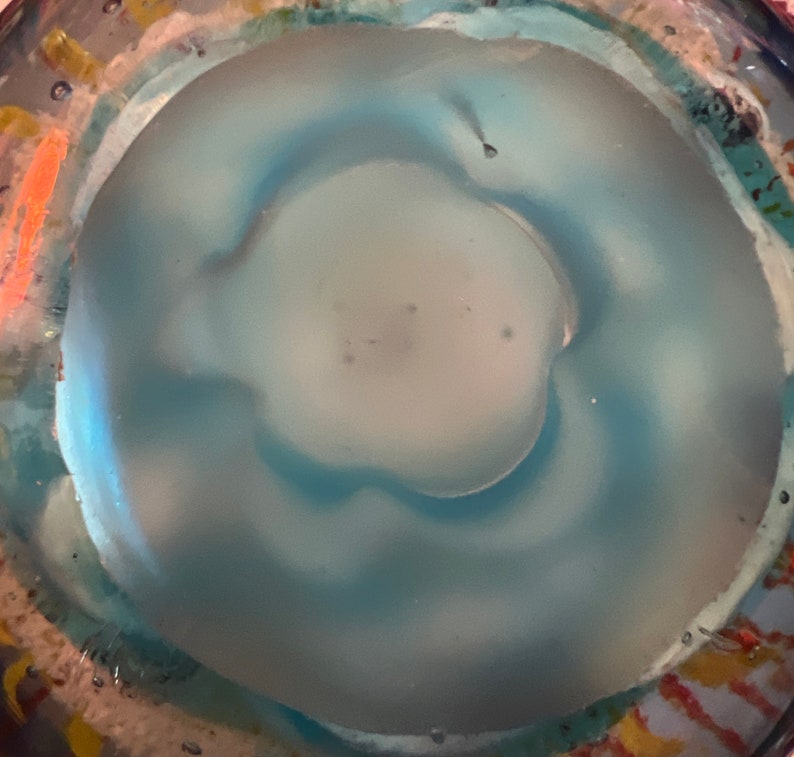 May include: A close-up of a blue glass bottle with a textured surface. The bottle has a clear, round opening at the top.