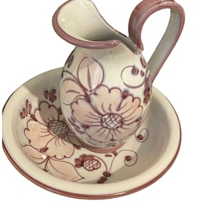 May include: A white ceramic jug with a pink floral design and a matching saucer. The jug has a handle and a spout. The saucer has a scalloped edge.