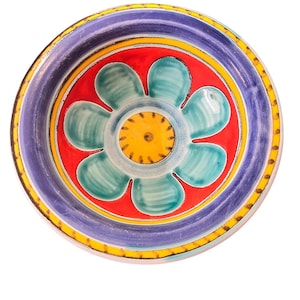 May include: A hand-painted ceramic plate with a floral design. The plate features a central flower with turquoise petals, a red background, and a purple rim. The rim is accented with yellow and black details. The plate is round.