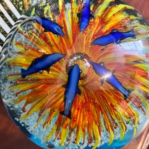 May include: A glass paperweight with a colorful flower design and blue dolphins swimming around it.