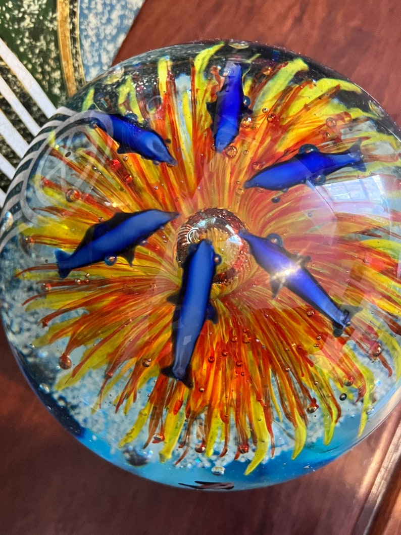 May include: A glass paperweight with a colorful flower design and blue dolphins swimming around it.