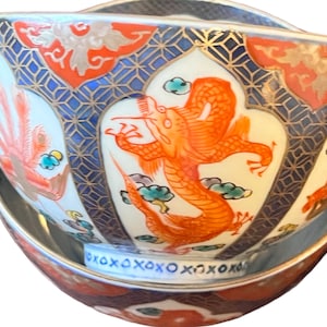 Puede incluir: Juego decorativo de cuenco y platillo de cer&aacute;mica. El cuenco presenta un vibrante dise&ntilde;o de drag&oacute;n naranja, patrones geom&eacute;tricos azules y detalles dorados. El platillo refleja el dise&ntilde;o del cuenco, creando un conjunto cohesivo y ornamentado. El conjunto es probablemente para servir o exhibir.