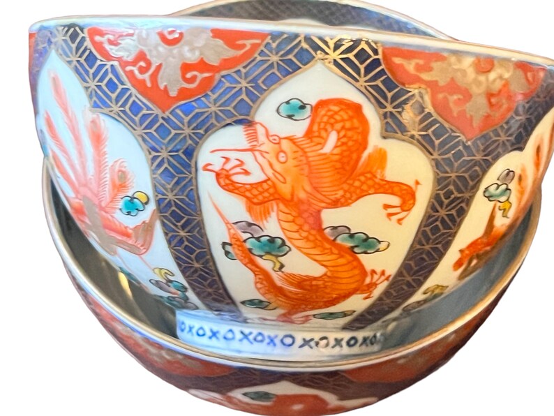 Puede incluir: Juego decorativo de cuenco y platillo de cer&aacute;mica. El cuenco presenta un vibrante dise&ntilde;o de drag&oacute;n naranja, patrones geom&eacute;tricos azules y detalles dorados. El platillo refleja el dise&ntilde;o del cuenco, creando un conjunto cohesivo y ornamentado. El conjunto es probablemente para servir o exhibir.