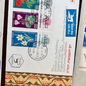 以下が含まれることがあります： アネモネ、シクラメン、スイセンなどの花が描かれたイスラエルの切手が付いた封筒。切手にはヘブライ語と英語の日付とテキストが刻印されています。封筒にはモザイクのボーダーデザインもあります。