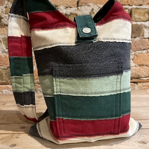 May include: A striped patchwork tote bag with a green strap and a silver button closure. The bag is made of different fabrics in shades of red, white, green, and black.