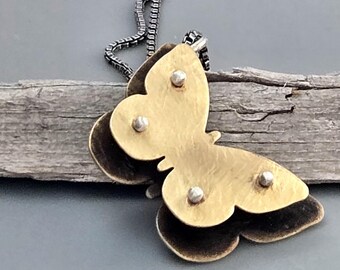 May include: A butterfly pendant necklace with a layered design. The top layer is gold-toned, and the bottom layer is dark brown. The pendant is attached to a silver-toned chain. The butterfly has three silver rivets.