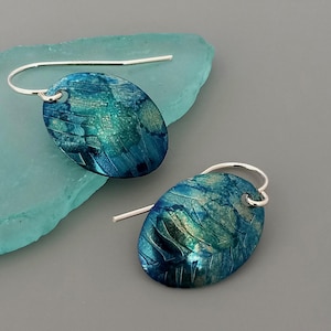 May include: A pair of silver dangle earrings with oval-shaped blue and green enamel pendants. The pendants have a textured, abstract design.