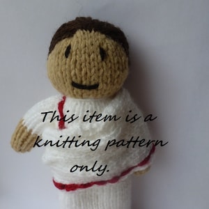May include: Knitting pattern for a doll with brown hair, a white sweater with red trim, and a tan face.
