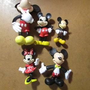 May include: A collection of Mickey Mouse and Minnie Mouse figurines. The figures are in various poses and sizes, with the iconic red, black, white, and yellow color scheme. One Mickey figure is wearing a tuxedo. The Minnie figure is wearing a red dress with white polka dots.