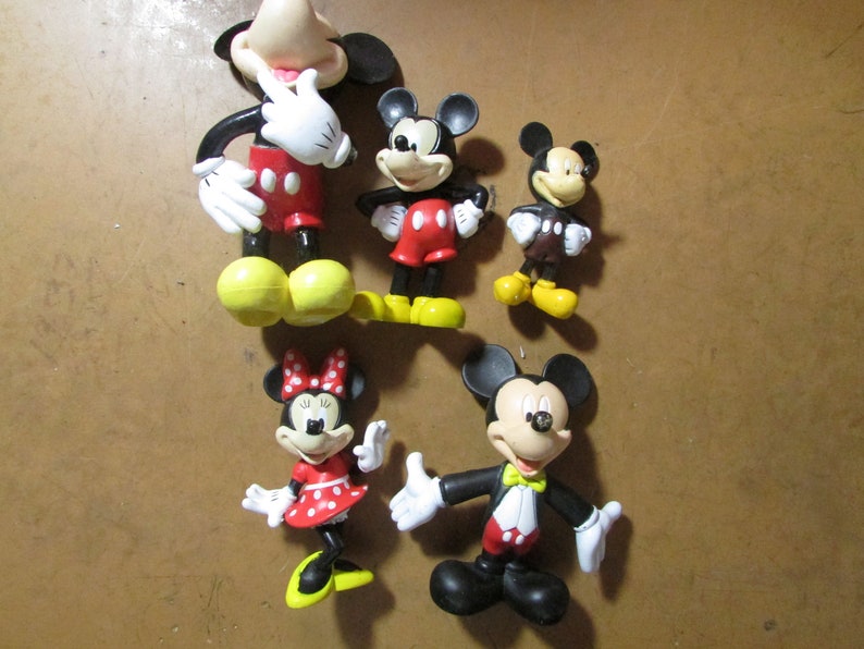 May include: A collection of Mickey Mouse and Minnie Mouse figurines. The figures are in various poses and sizes, with the iconic red, black, white, and yellow color scheme. One Mickey figure is wearing a tuxedo. The Minnie figure is wearing a red dress with white polka dots.