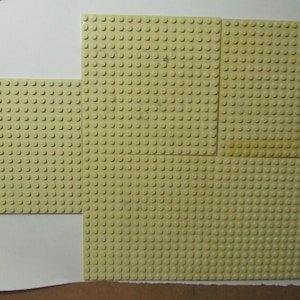May include: Several light tan building block baseplates of varying sizes are arranged together. The baseplates have a grid of raised studs for attaching building blocks. The arrangement suggests a construction or building project.
