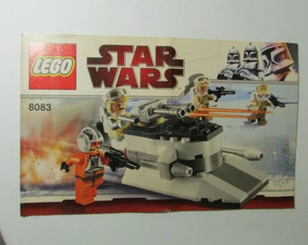 May include: Lego Star Wars set 8083 featuring a white and gray vehicle with black detailing. The set includes several Lego figures in orange and tan uniforms, armed with black blasters. The Star Wars logo is visible.