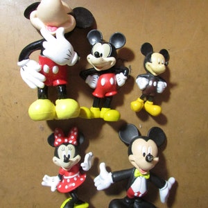 May include: A collection of five Mickey Mouse and Minnie Mouse figurines. The figurines feature the iconic characters in various poses, with black, red, white, and yellow color schemes. The figurines are made of a glossy material.