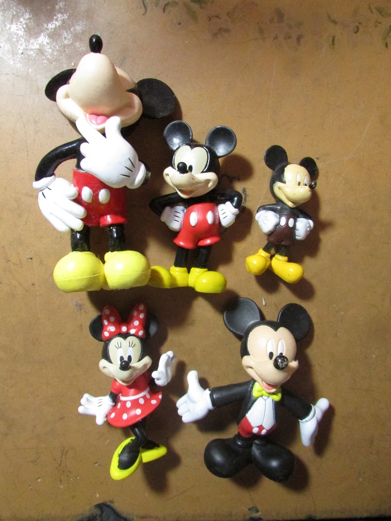 May include: A collection of five Mickey Mouse and Minnie Mouse figurines. The figurines feature the iconic characters in various poses, with black, red, white, and yellow color schemes. The figurines are made of a glossy material.