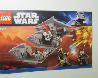 May include: LEGO Star Wars set 7957 box art. The image shows a gray spaceship with red lightsabers and minifigures. The LEGO and Star Wars logos are visible, along with the set number.
