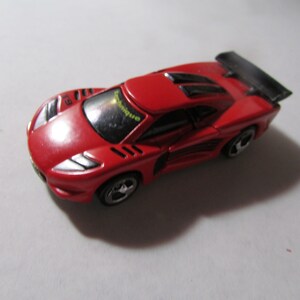 May include: A red toy sports car with black accents, including a rear spoiler. The car has silver wheels and the word "technique" is visible on the windshield. The car is a miniature model.