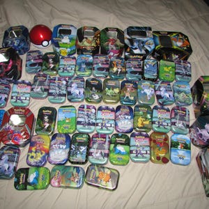 May include: A collection of various Pokémon-themed tins and a Poké Ball. The tins feature colorful illustrations of Pokémon characters and logos. The tins are rectangular and square, with hinged lids. The Poké Ball is red and white.