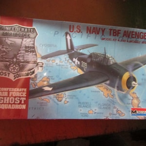 May include: A model kit box for a U.S. Navy TBF Avenger aircraft. The box features a dark blue airplane illustration with a yellow propeller and the text "U.S. NAVY TBF AVENGER". The box also includes the text "Confederate Air Force Ghost Squadron".