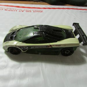 May include: A toy sports car in cream, black, and green. The car has a spoiler and the number 12 on the side. The text "MII PROTOTYPE" is also visible. The car is a die-cast model.