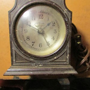 May include: An antique brown electric clock with a round face and a dark frame. The clock face has black numbers and hands, with the brand name "Lincoln" visible. A power cord is attached to the side. The clock is likely from the mid-20th century.