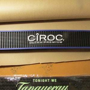 May include: A rectangular bar mat with a blue border and a black, textured surface. The mat features the white "CÎROC ULTRA PREMIUM" logo. The mat is designed for use in a bar setting.
