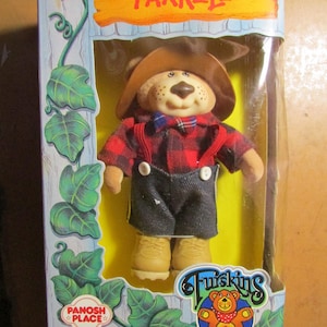 May include: A Farrell doll in its original packaging. The doll is a bear wearing a brown hat, red plaid shirt, suspenders, and denim shorts. The packaging includes the text "Panosh Place" and "For ages 3 and up."