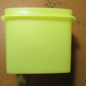 May include: A bright neon yellow plastic storage container with a rectangular shape and a matching lid. The container features smooth, matte surfaces and a slightly flared rim at the top, providing a simple and functional design for storage.