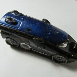 May include: A vintage toy car with a streamlined design. The car features a dark blue top and a black body with silver accents. It has four wheels and a small hook at the front.