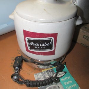 May include: A white ceramic buffet patio server with a lid, featuring a "Black Label Beer" logo. The server has a black power cord and sits on a metal base. A West Bend tag is visible.