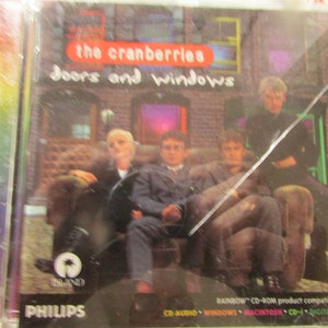 May include: CD case for "Doors and Windows" by The Cranberries. The album cover features the band members seated on a couch. The title is in red, and the band's name is in white. The Island and Philips logos are visible.