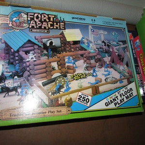 May include: A vintage "Fort Apache" frontier play set box. The box features a colorful illustration of a fort, figures, and a play mat. The set includes over 250 pieces and a 27" x 72" play mat. The box has text that reads "General Custer" and "Traditional Frontier Play Set."