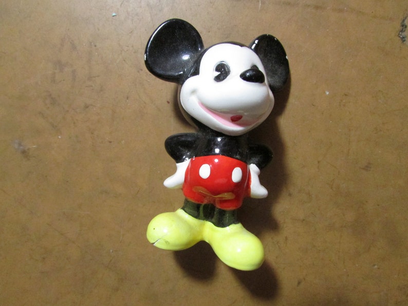 May include: A ceramic figurine of Mickey Mouse, featuring black ears, a white face, and a red shorts. The figure has yellow shoes and white gloves, with a smiling expression. A classic Disney collectible.