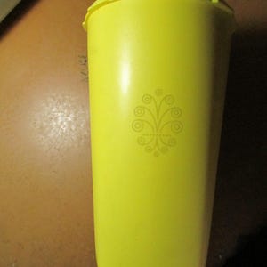 May include: A bright yellow plastic tumbler with a matching lid. The tumbler has a decorative floral design on the front. The tumbler is cylindrical and appears to be about 7 inches tall.