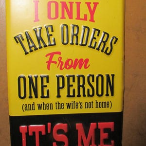 May include: A rectangular yellow sign with black and red text. The sign reads "I ONLY TAKE ORDERS From ONE PERSON (and when the wife's not home) IT'S ME."