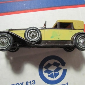 May include: A vintage yellow and black toy car with a convertible top. The car has detailed wheels and a spare tire. The model car is a classic design, likely from the mid-20th century.