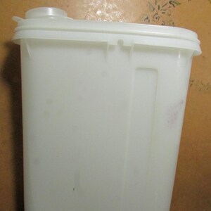 May include: A white plastic container with a rectangular shape and a lid. The container has a handle and a spout on top. The container is made of a durable plastic material.