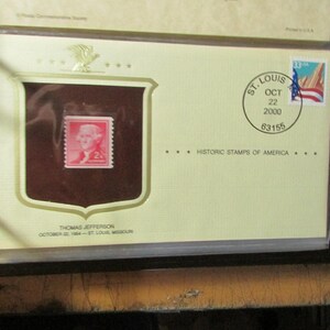 May include: A historic stamp of Thomas Jefferson, encased in a protective sleeve. The stamp is red with a portrait of Jefferson. The envelope is cream-colored with a St. Louis postmark dated October 22, 2000. The text "Historic Stamps of America" is printed below.