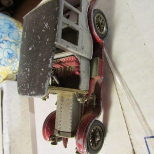 May include: A vintage toy car with a red and silver body, black wheels, and a black roof. The toy car has a detailed interior and shows signs of wear, suggesting it is an antique or collectible item.