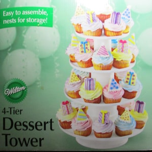 May include: A white 4-tier dessert tower with cupcakes decorated with frosting, gift boxes, and party hats. The box reads "Easy to assemble, nests for storage!" and "4-Tier Dessert Tower" with the Wilton logo.