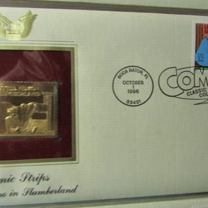 May include: A framed collectible featuring a gold-colored stamp with an illustration from "Little Nemo in Slumberland." The frame includes a stamp with the text "Little Nemo - Slumberland" and the word "COMICS" with "Classic Collection" below it. The text "Comic Strips Little Nemo in Slumberland" is also visible.