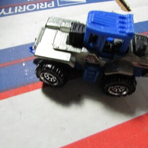 May include: A die-cast metal toy truck with a silver body and a blue cab. The truck has black wheels with detailed tire treads. The toy is on a white, blue, and red surface.