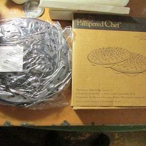 May include: A new, unopened Microwave Chip Maker set of 2 from The Pampered Chef. The box is tan with a drawing of the chip makers. The chip makers are in a clear plastic bag.