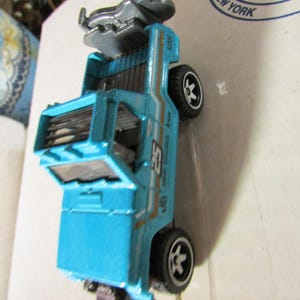 May include: A turquoise toy truck with black wheels and a silver accessory on top. The truck has white and gold stripes and the number 25 on the side. The text "SWT" is visible on the side of the truck.