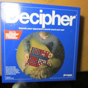 May include: A blue Decipher board game box featuring the title in large white letters. The box displays a circular image of two players using a game board with red and white tiles. Text includes 'Decode your opponent's secret word and win!' and 'Pressman'.