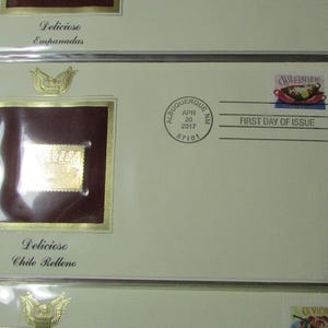 May include: A collection of envelopes featuring stamps and the text "Delicioso Empanadas" and "Delicioso Chile Relleno." Each envelope has a gold-colored stamp and a decorative emblem. The envelopes are cream-colored with a "First Day of Issue" stamp.