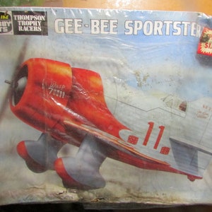 May include: A vintage model airplane kit, the Gee-Bee Sportster, is packaged in a clear plastic wrap. The box features a red and silver airplane illustration with the number 11. The text "LIFE-LINE HOBBY KITS" and "THOMPSON TROPHY RACERS" are visible.