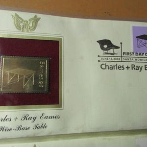 May include: A commemorative envelope featuring a gold-colored stamp with a wire-base table design. The envelope includes the text "Charles + Ray Eames" and "Wire-Base Table". A purple stamp with a table design and the text "First Day of Issue" is also present.