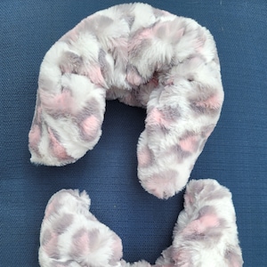 May include: A plush, U-shaped neck pillow and a smaller, matching piece. The pillow features a soft, faux fur fabric in a pattern of white, gray, and pink spots. The items are designed for comfort and support.