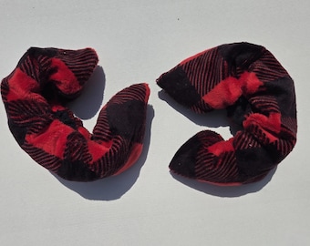 May include: Two plush, U-shaped neck pillows in a red and black buffalo plaid pattern. The pillows are made of a soft, fuzzy material and are designed to provide support and comfort. The pillows are ideal for travel or home use.