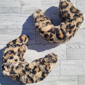 May include: Two brown and black leopard print faux fur neck warmers. The neck warmers are shaped like a crescent moon.